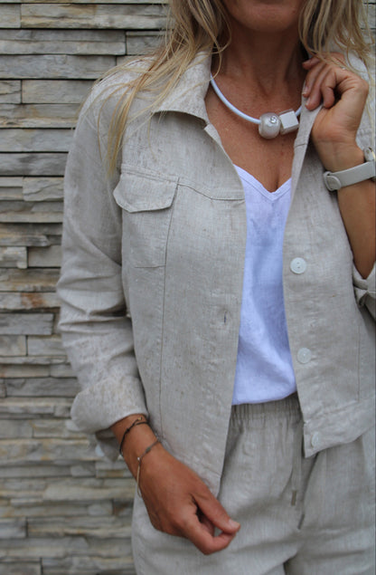 Person wearing a light natural jacket and white tank top against a stone wall.